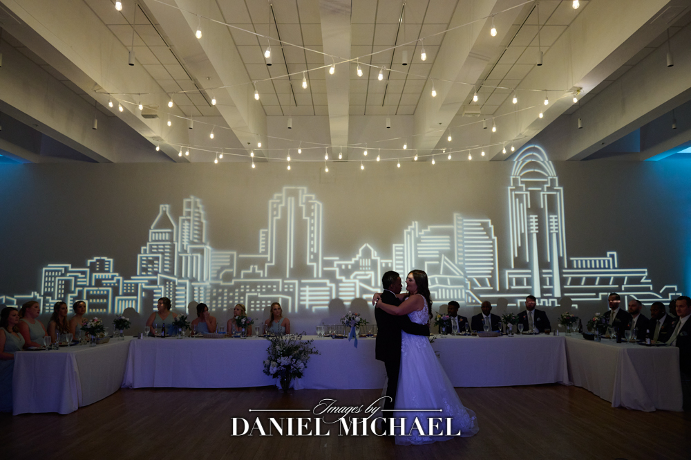Couple dancing in front of wedding party table and city silhouette
