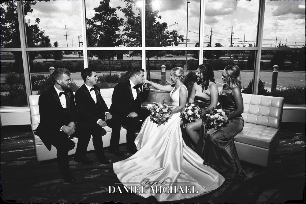 Wedding party sitting on chairs with groom kissing bride's hand